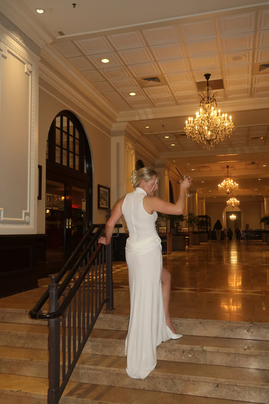 Woman in a white dress standing in a room with wooden paneling and chandeliers.