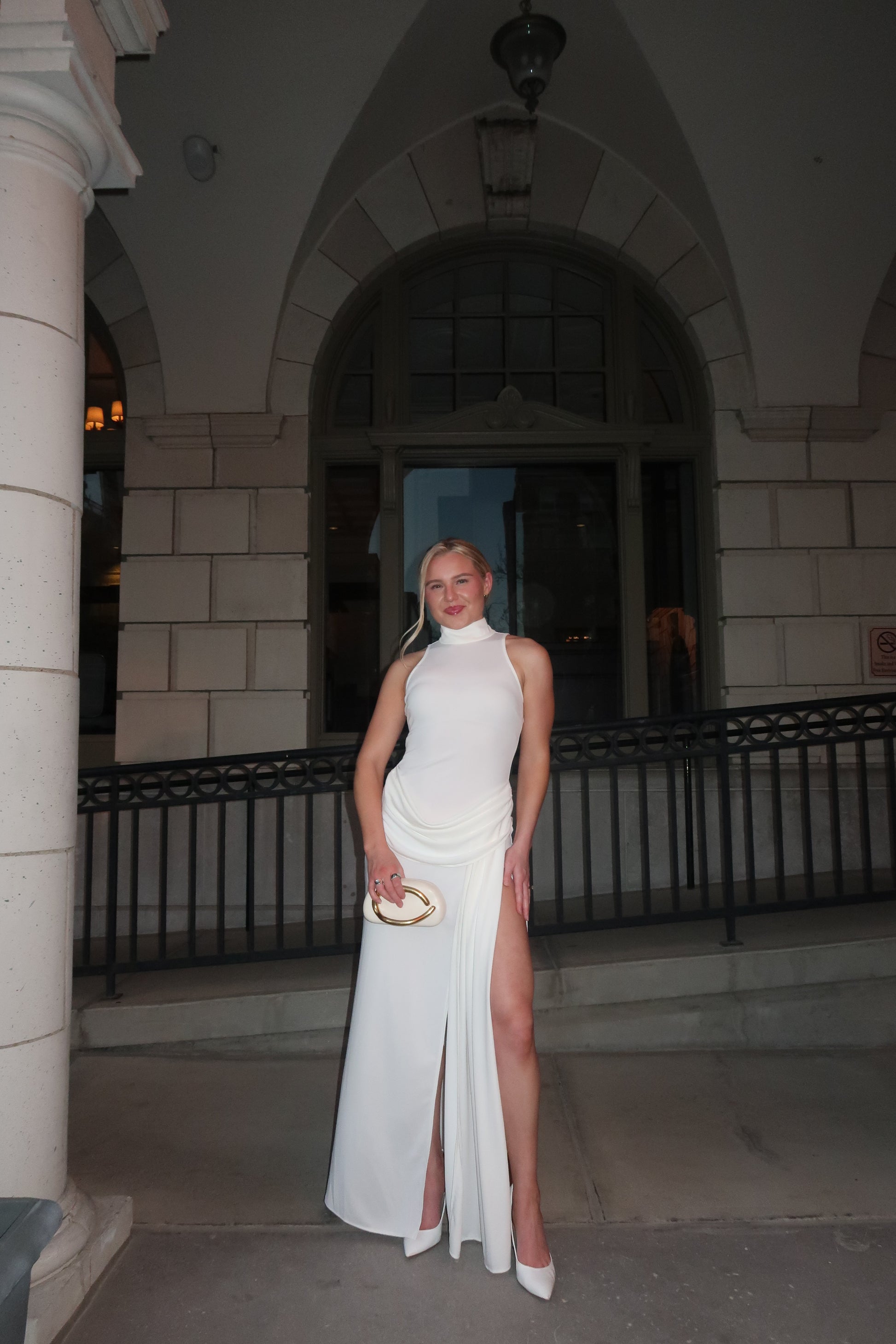 Woman in a white dress standing in an architectural setting with columns and steps.