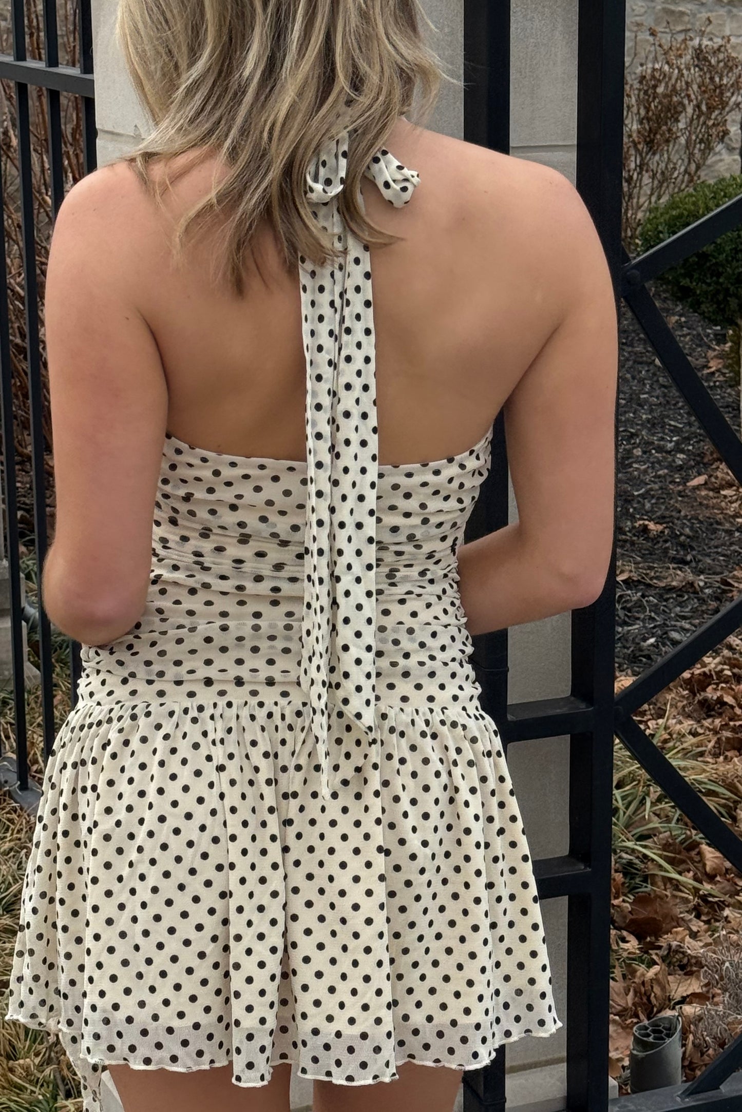 Woman wearing a polka dot dress with a black metal gate in the background