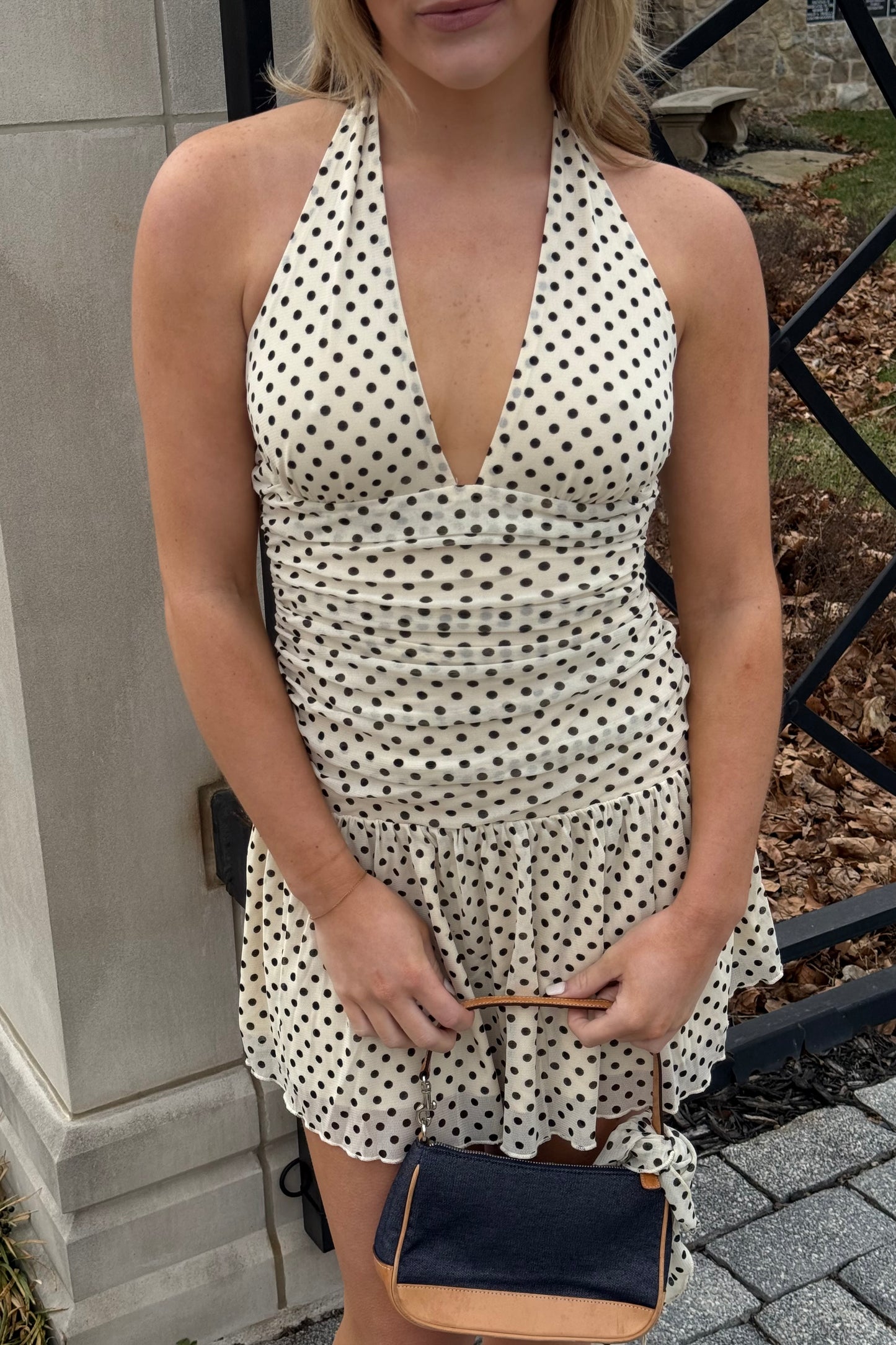Woman wearing a polka dot dress holding a small bag outdoors.