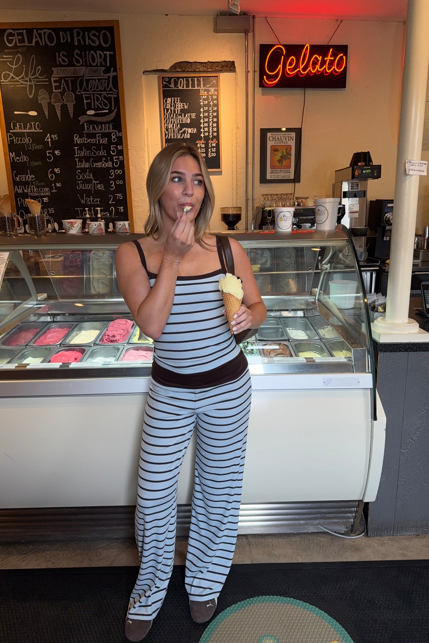 Woman in a striped outfit eating ice cream at a gelato shop.