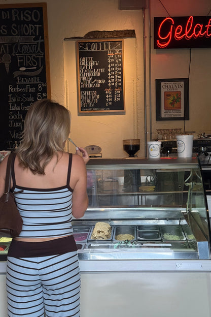 Woman standing in front of a gelato display case with a neon sign in the background.