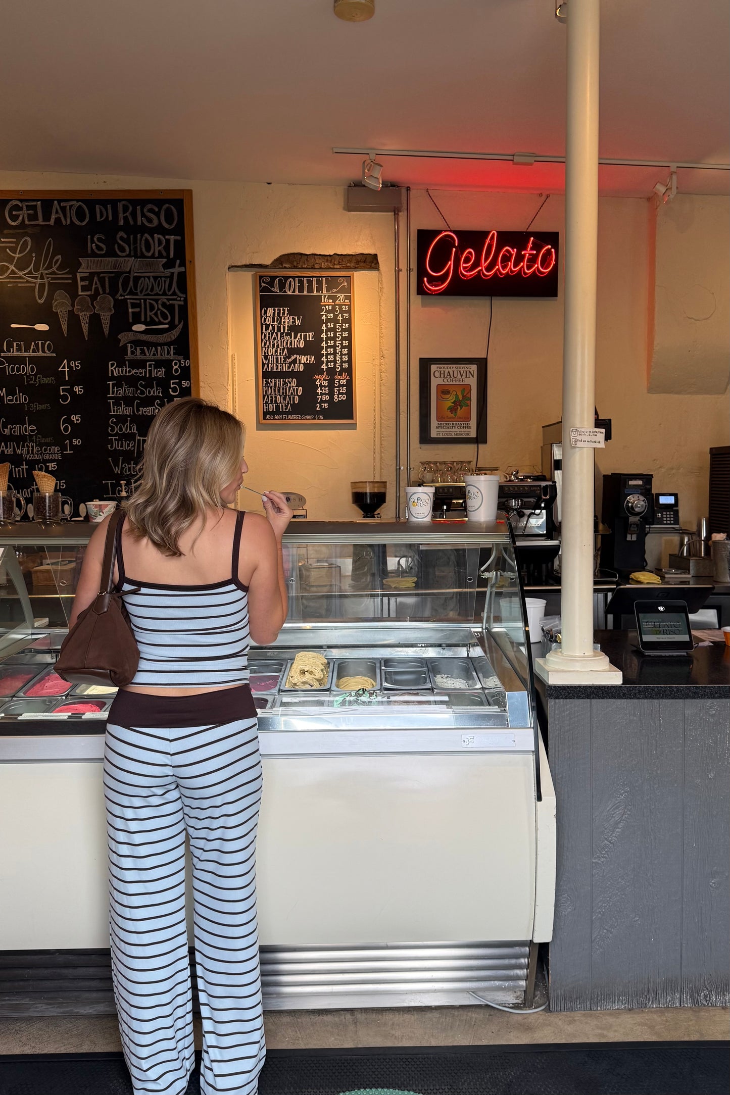 Woman standing in front of a gelato display case with a 'Gelato' sign above.