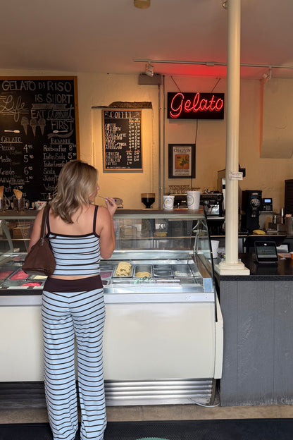 Woman standing in front of a gelato display case with a 'Gelato' sign above.