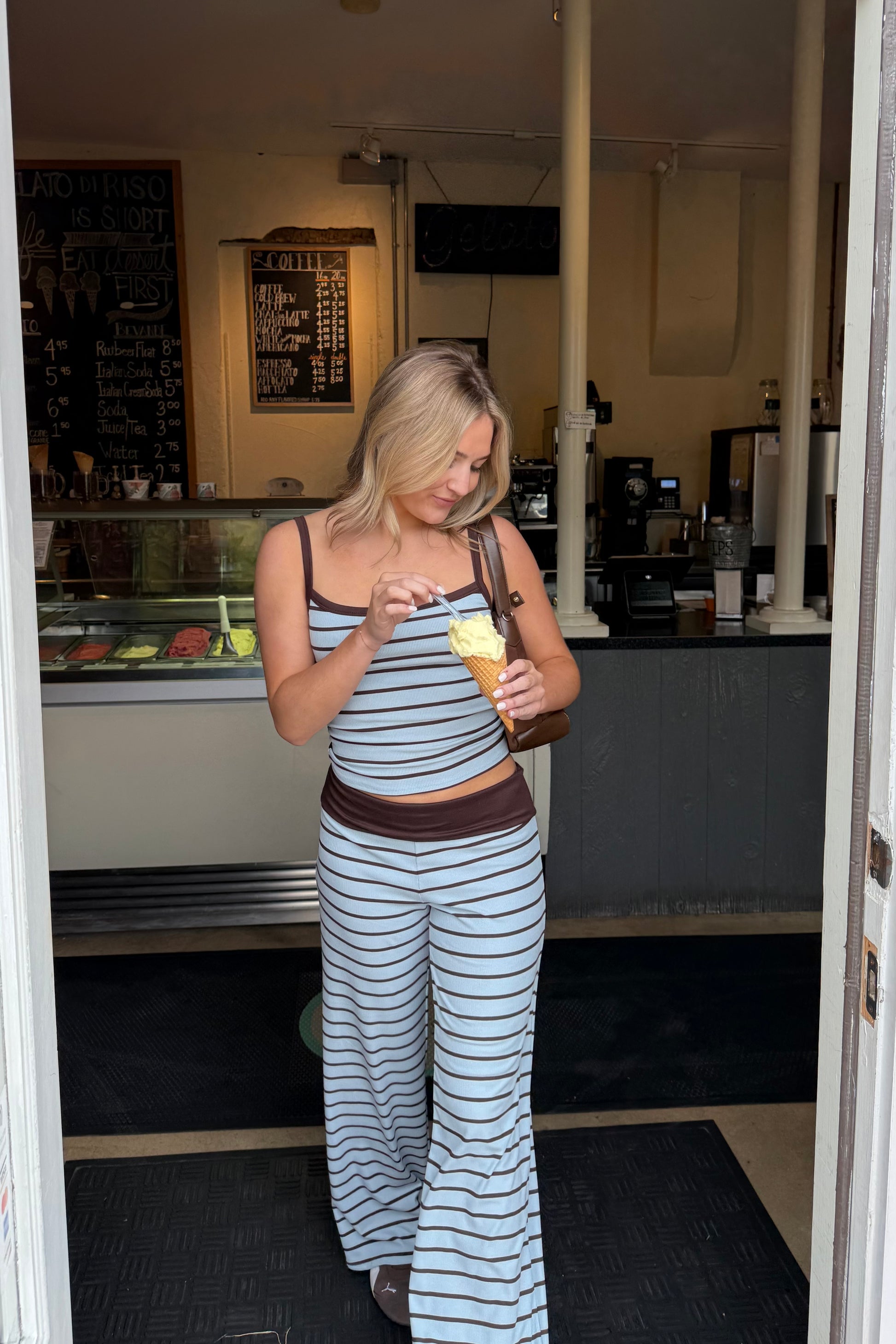 Woman in a striped outfit standing in a casual setting, possibly a cafe or store.