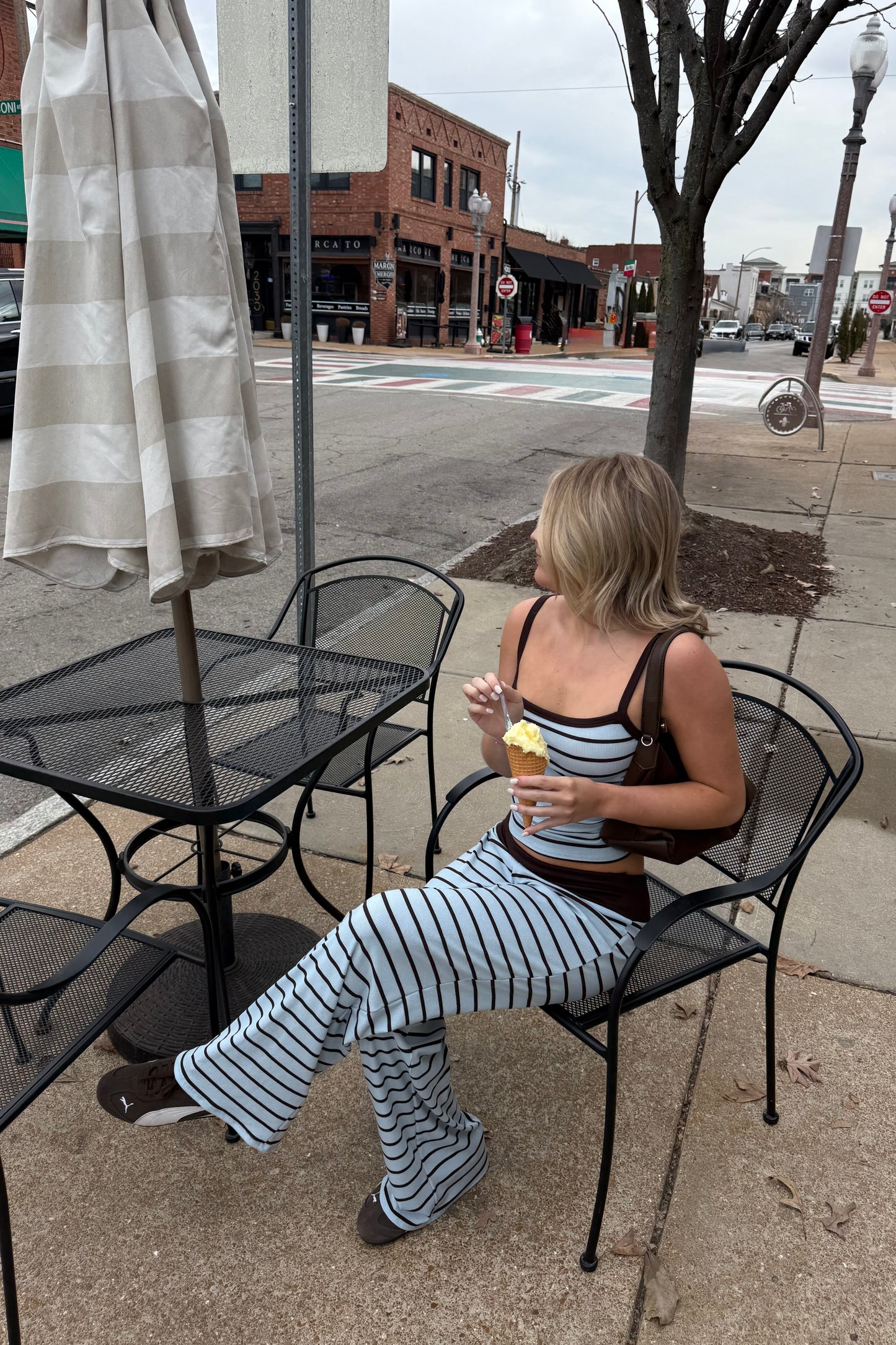 Woman sitting at an outdoor cafe table eating a ice cream cone on a city street.