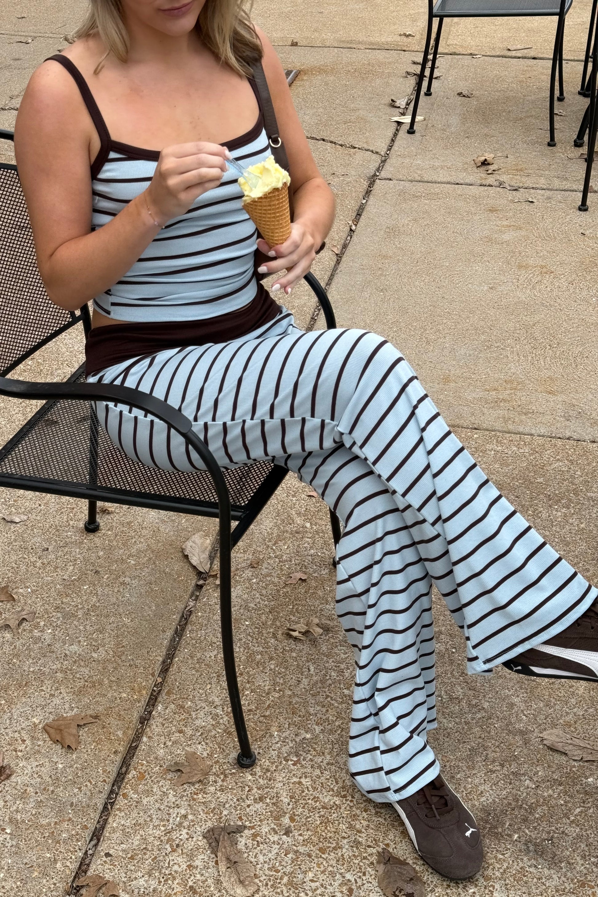 Woman in a striped outfit sitting outdoors eating ice cream.