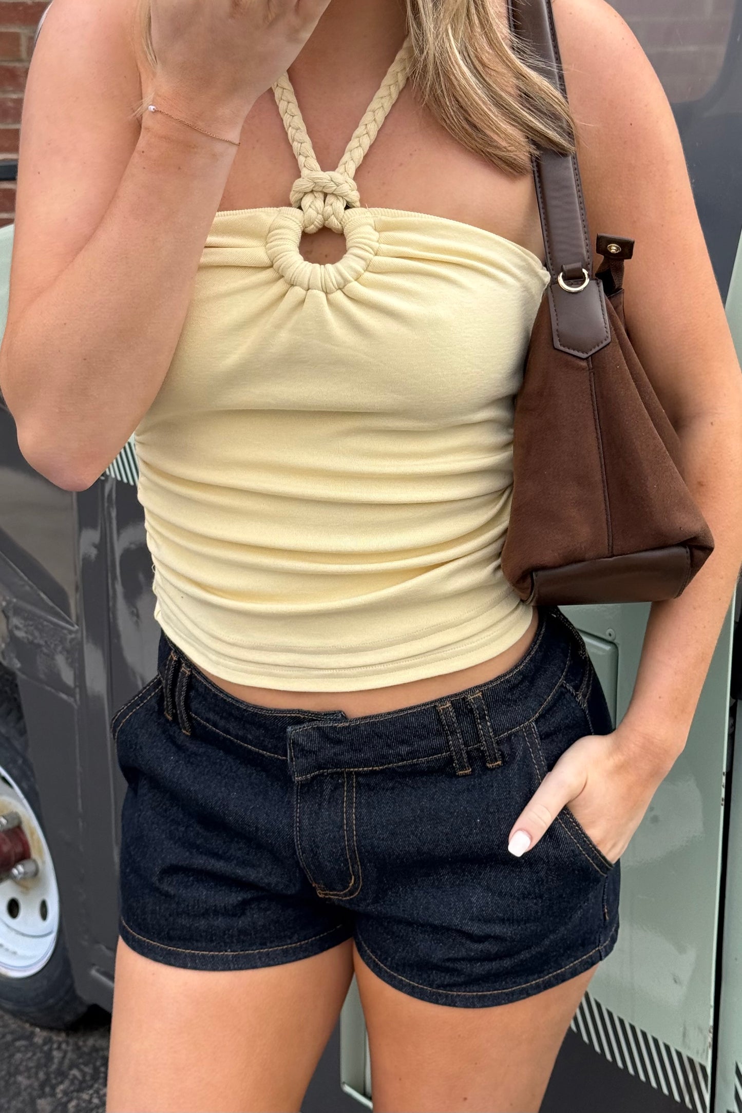 Woman wearing a yellow halter top and dark shorts, standing next to a vehicle.