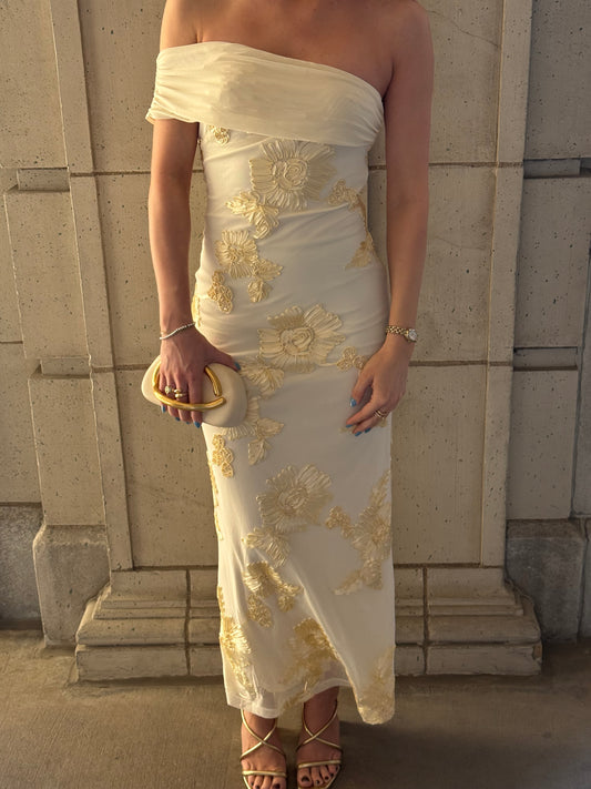 Woman wearing a white dress with gold embroidery standing on stone steps.