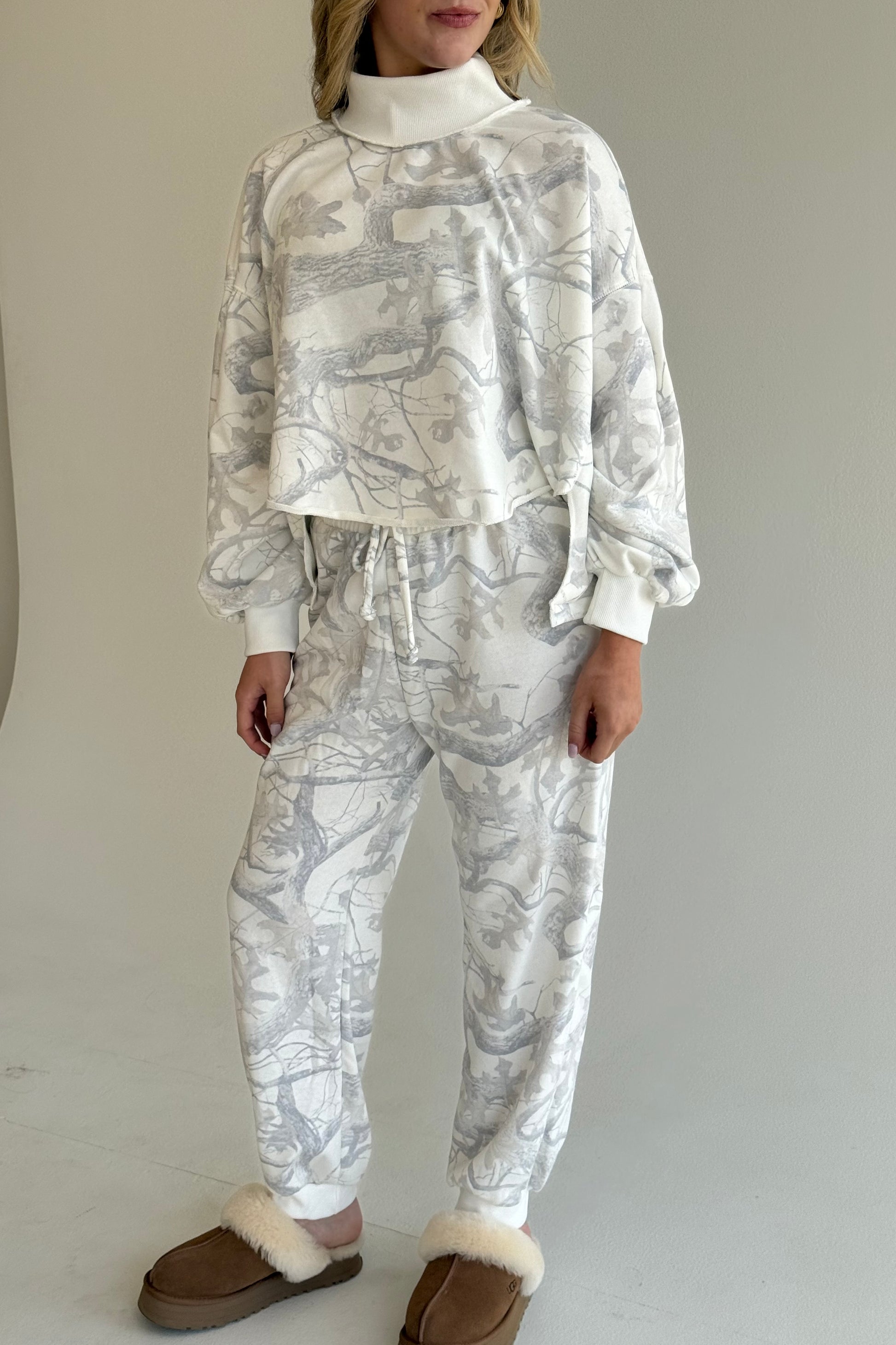 Person wearing a white and gray patterned outfit with brown slippers on a plain background