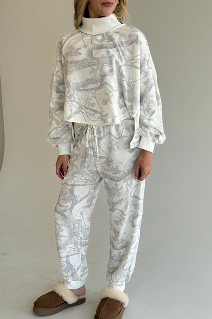 Person wearing a white and gray patterned outfit with brown slippers on a plain background