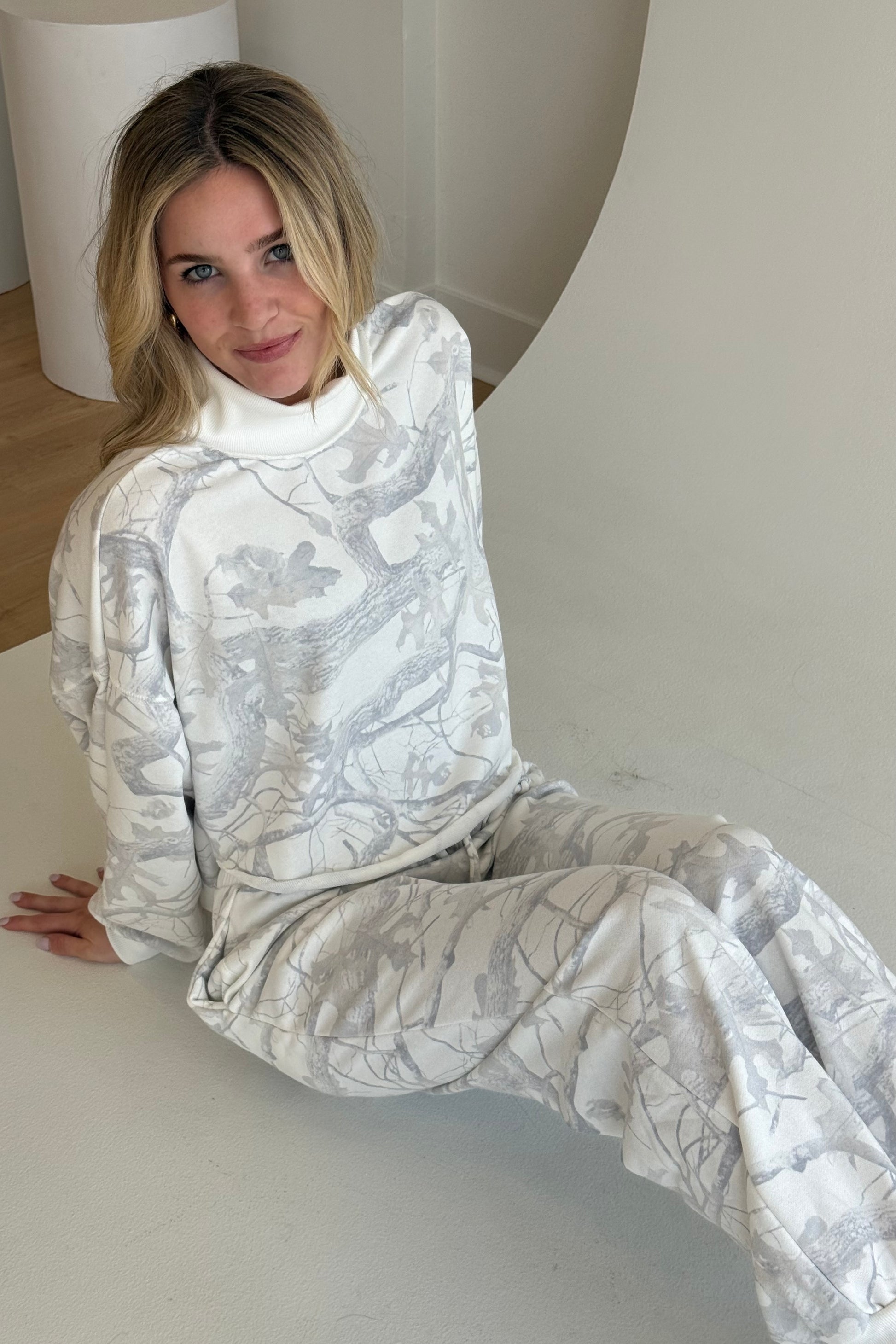 Woman wearing a white patterned outfit sitting on a white surface.