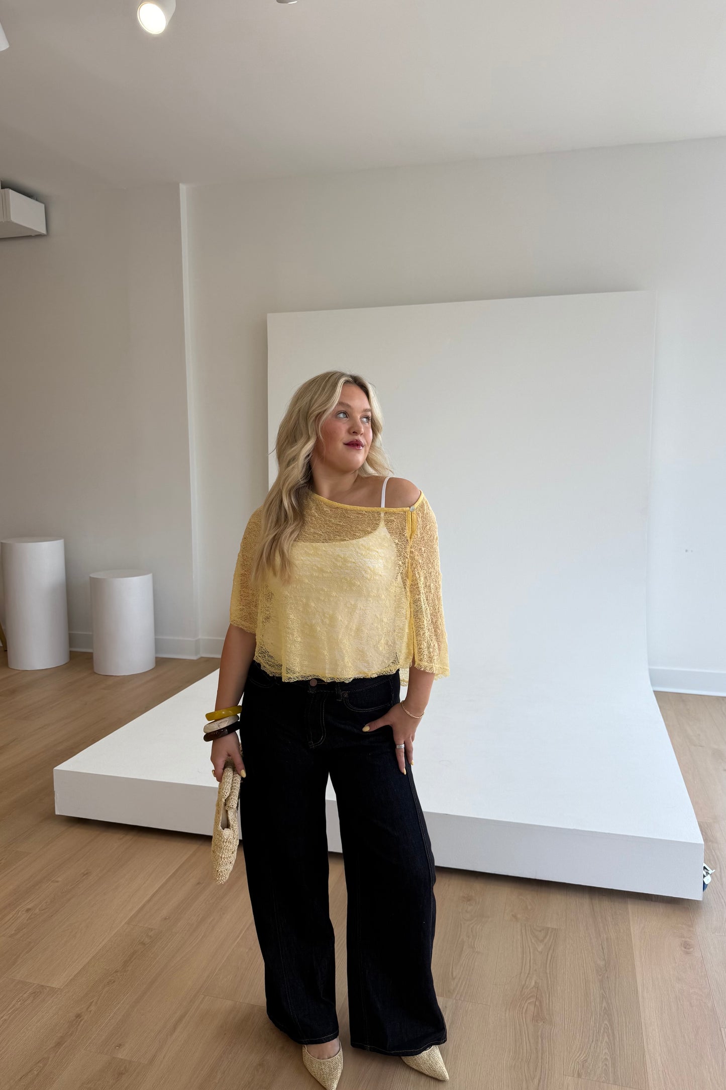Woman in a yellow top and black pants standing in a studio setting.
