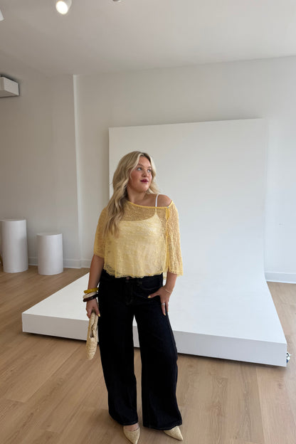 Woman in a yellow top and black pants standing in a studio setting.