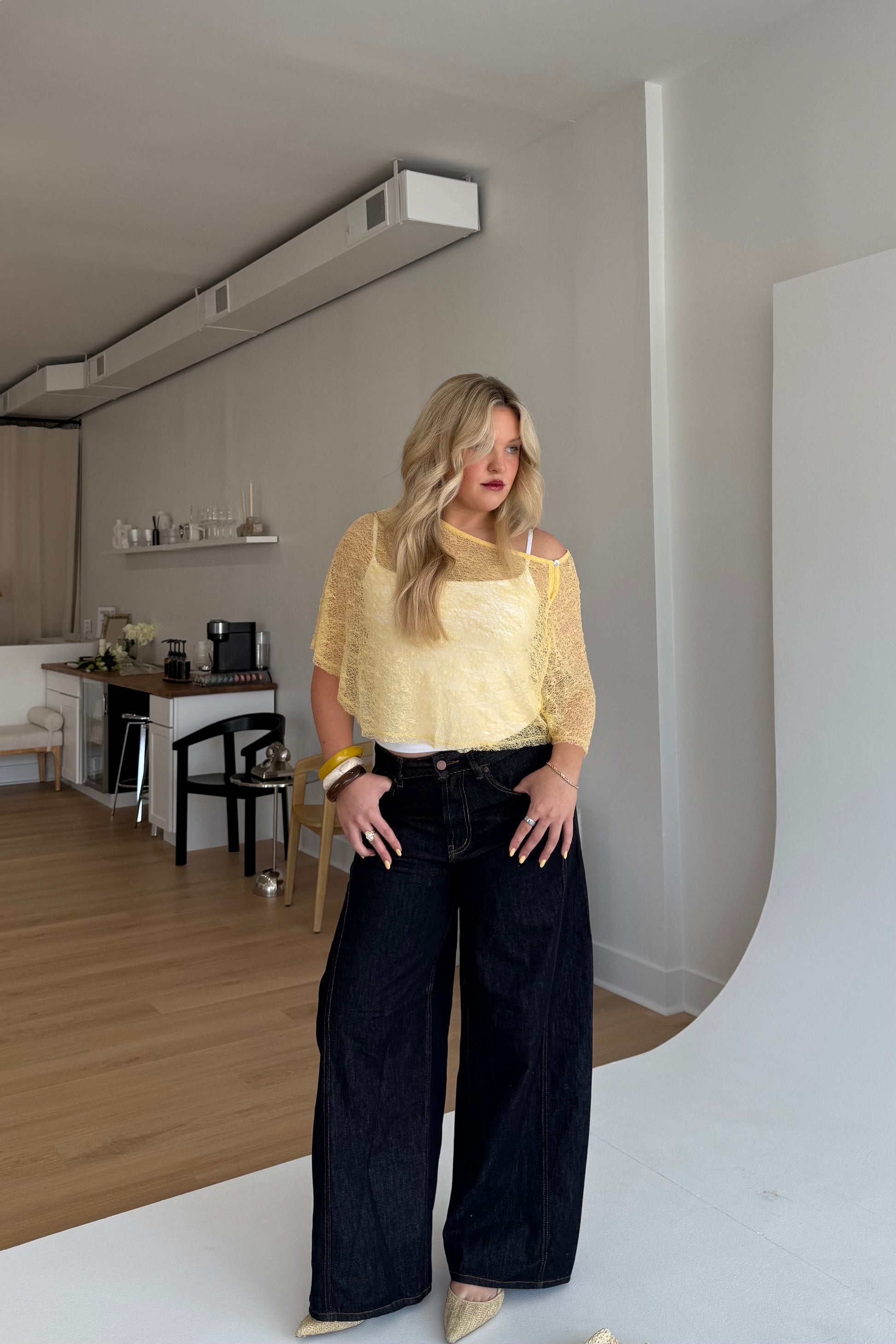 Woman in a yellow top and black pants standing in a room with a white backdrop