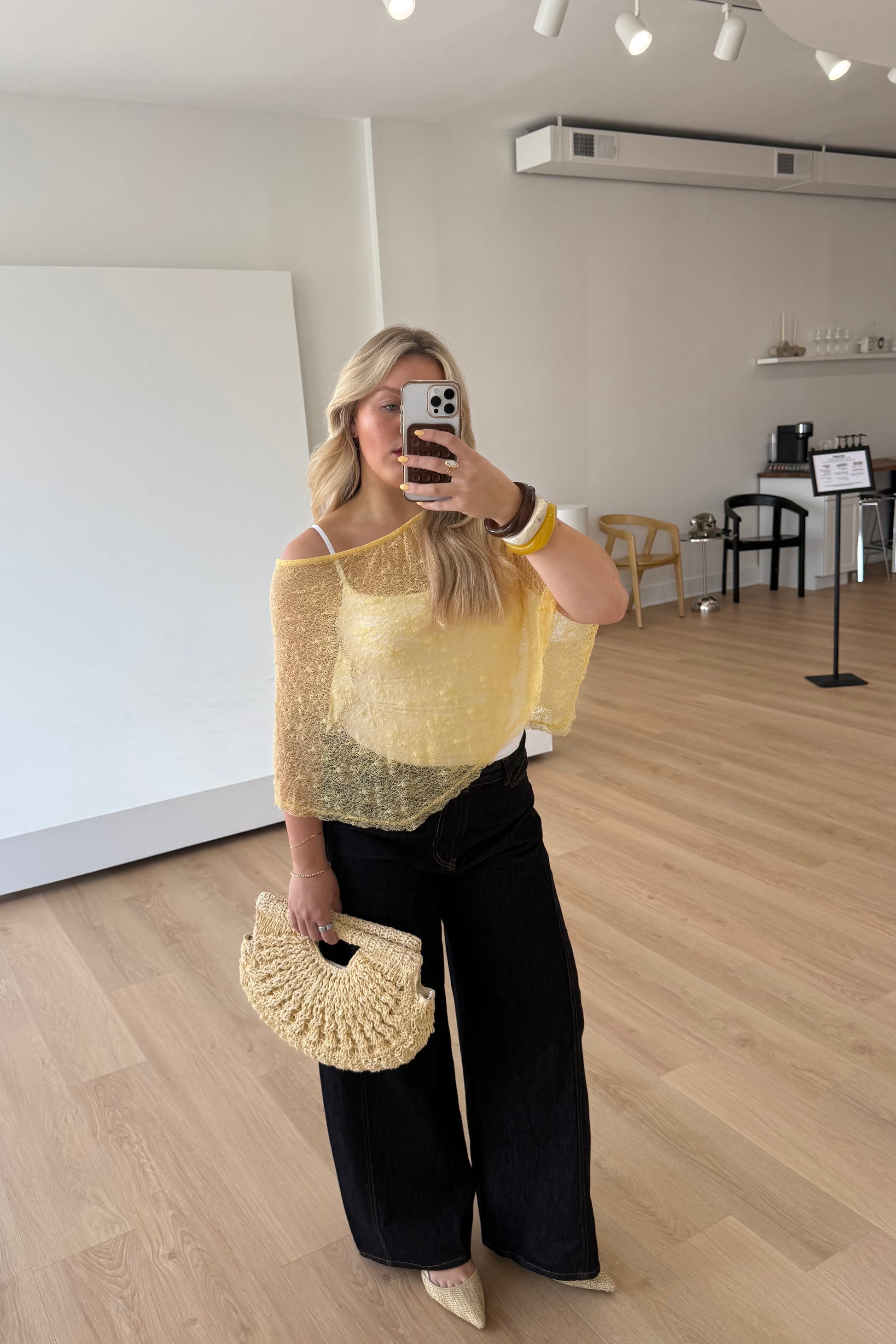 Woman in yellow top and black pants taking a mirror selfie in an indoor setting.