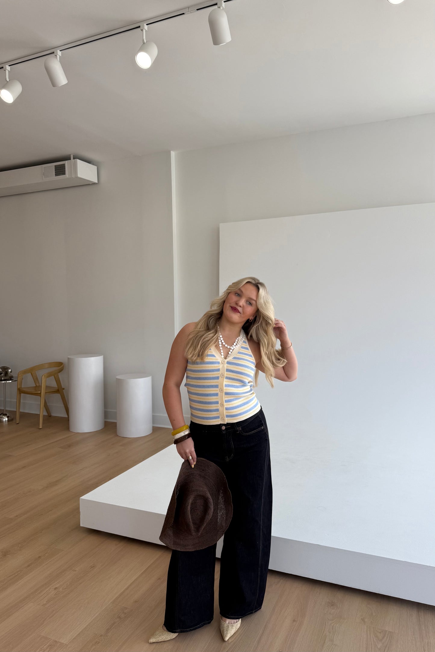 Woman posing in a modern indoor setting holding a hat