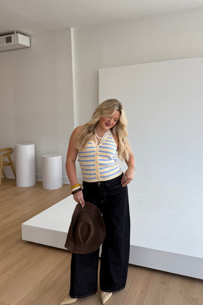 Woman holding a hat in a minimalistic room with white walls and wooden floor.