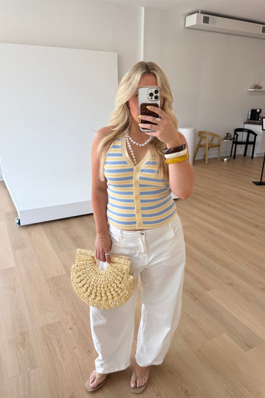 Woman taking a mirror selfie wearing a striped top and white pants in a room with wooden flooring.