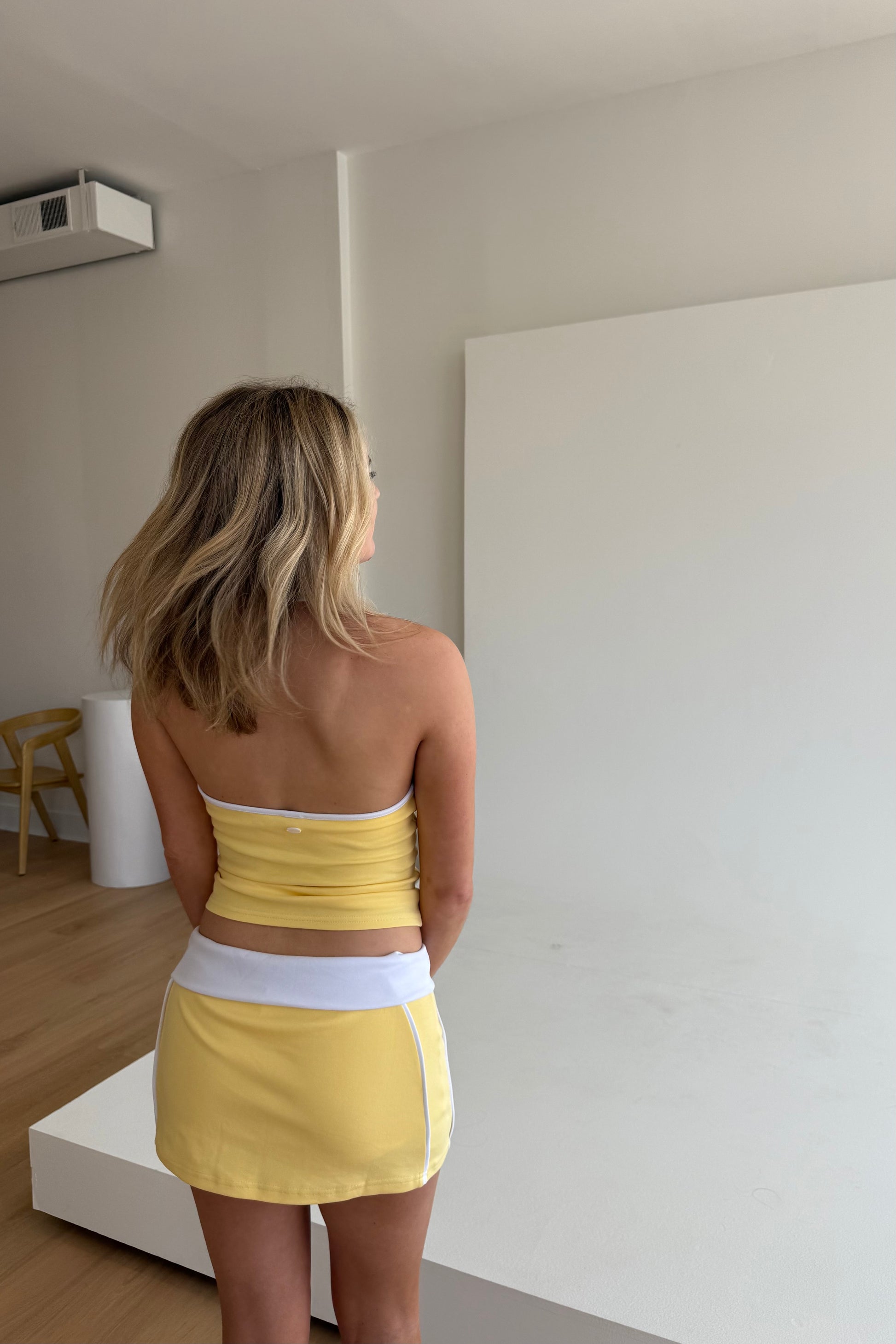 Woman wearing a yellow and white outfit standing in a minimalistic room.