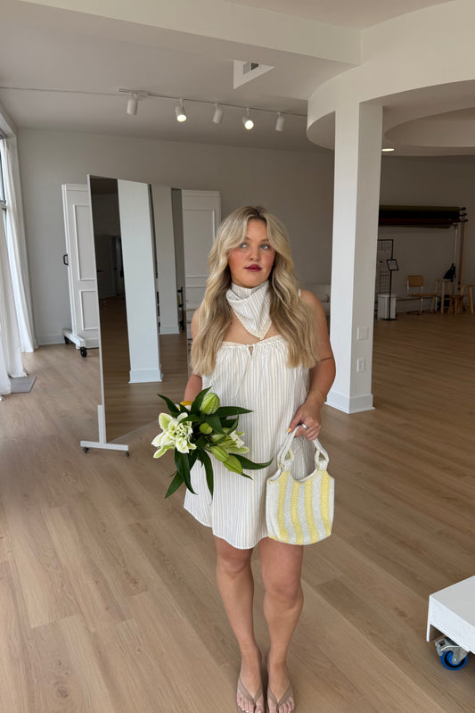 Woman in a white dress holding flowers and a yellow bag in an indoor setting