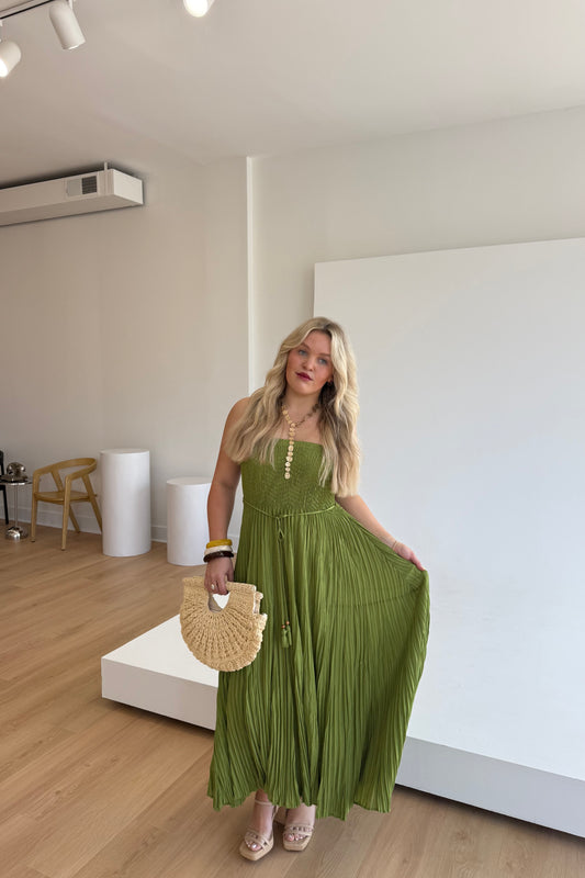 Woman in a green dress holding a straw bag in a minimalistic room.