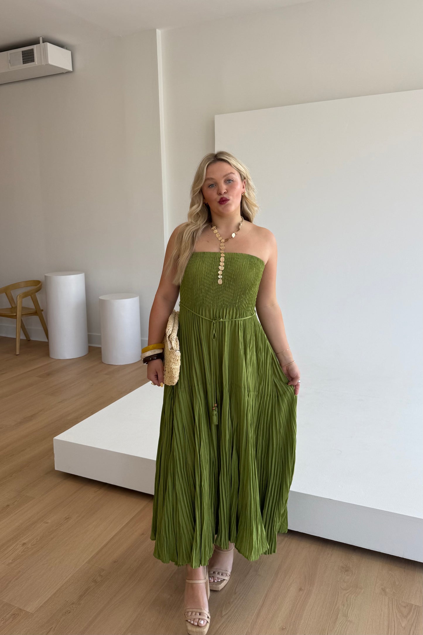 Woman in a green strapless dress standing in a minimalistic room with white walls and wooden floor.