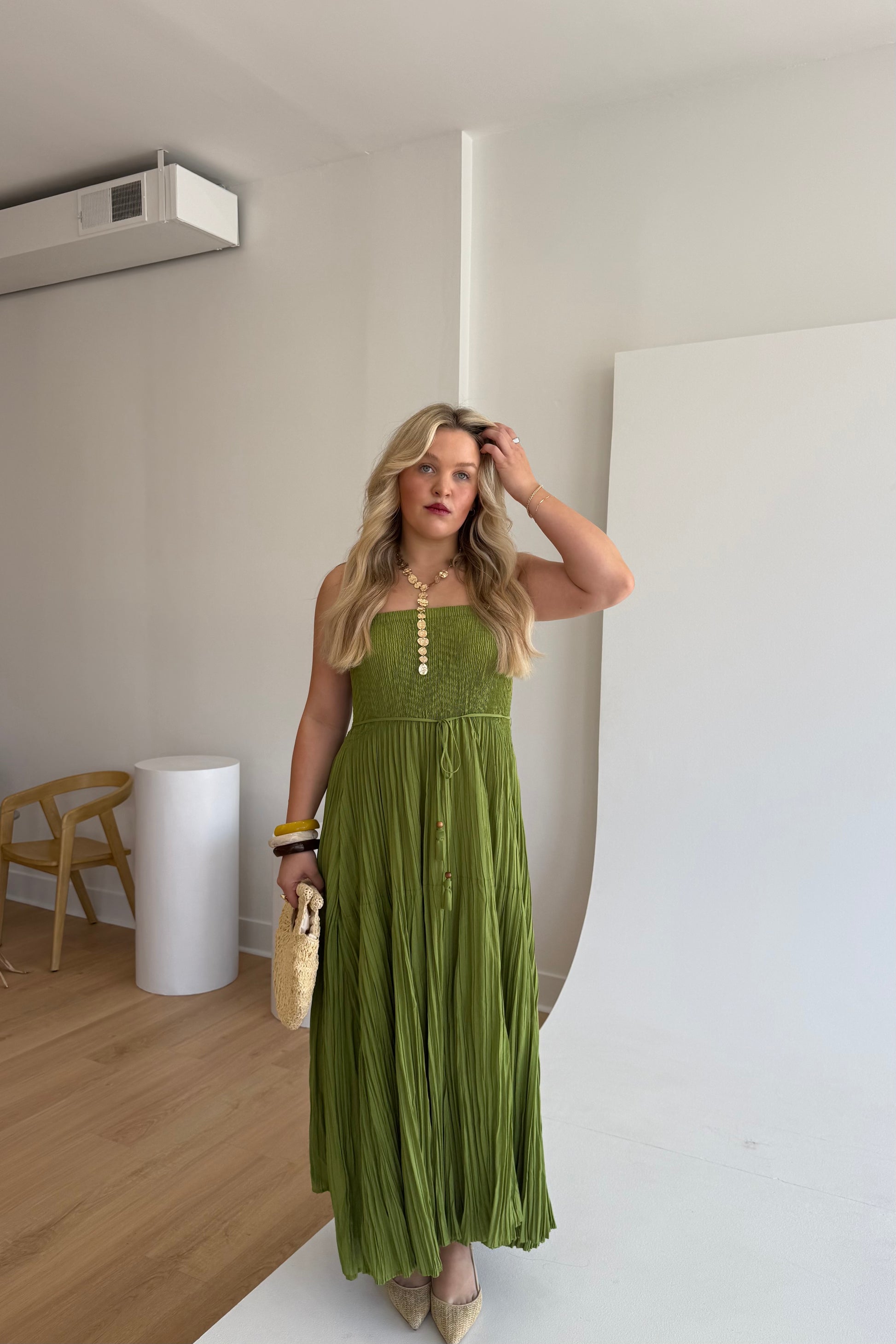 Woman in a green dress standing in a room with wooden floor and white walls.