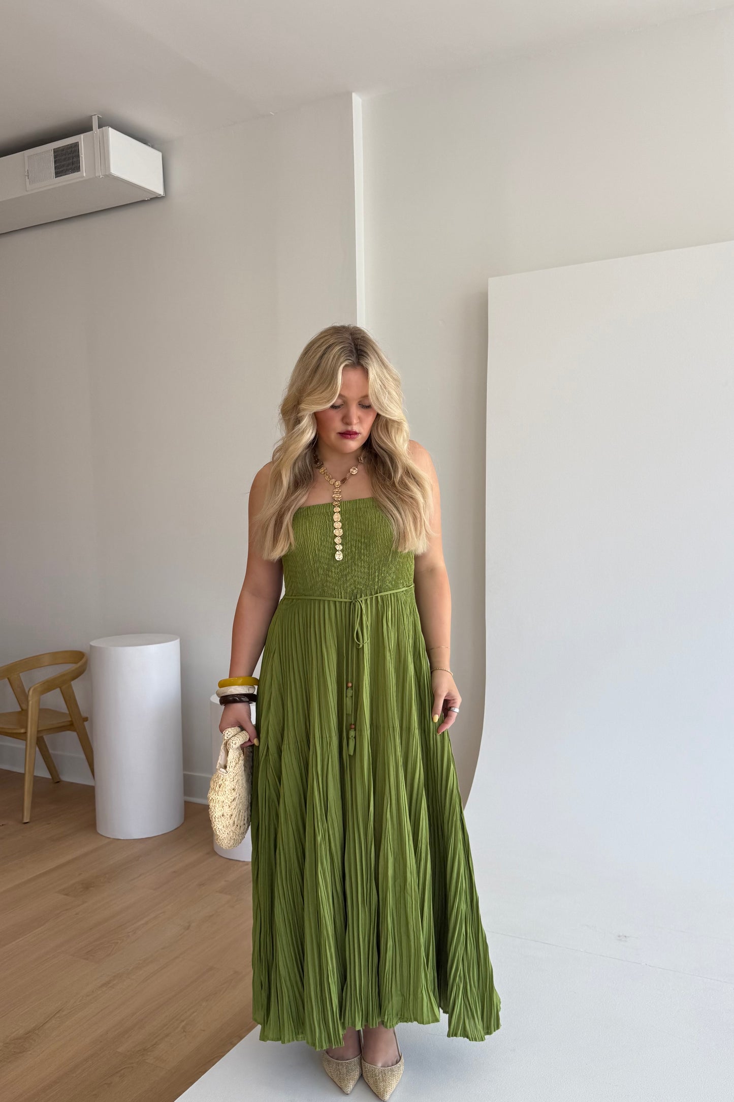 Woman in a green dress standing in a room with wooden floor and white walls.