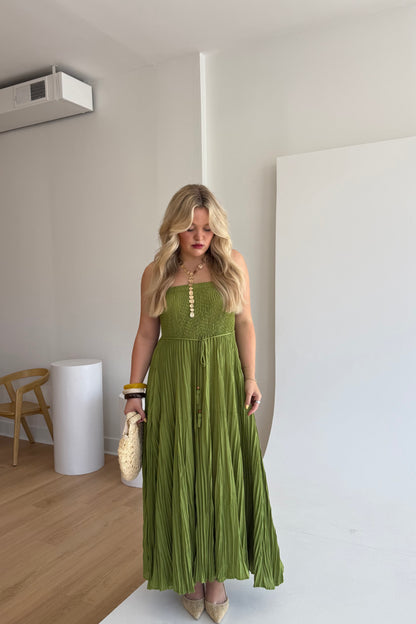 Woman in a green dress standing in a room with wooden floor and white walls.