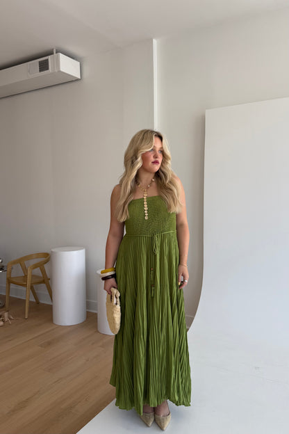 Woman in a green dress standing in a minimalistic room with white walls and wooden floor.
