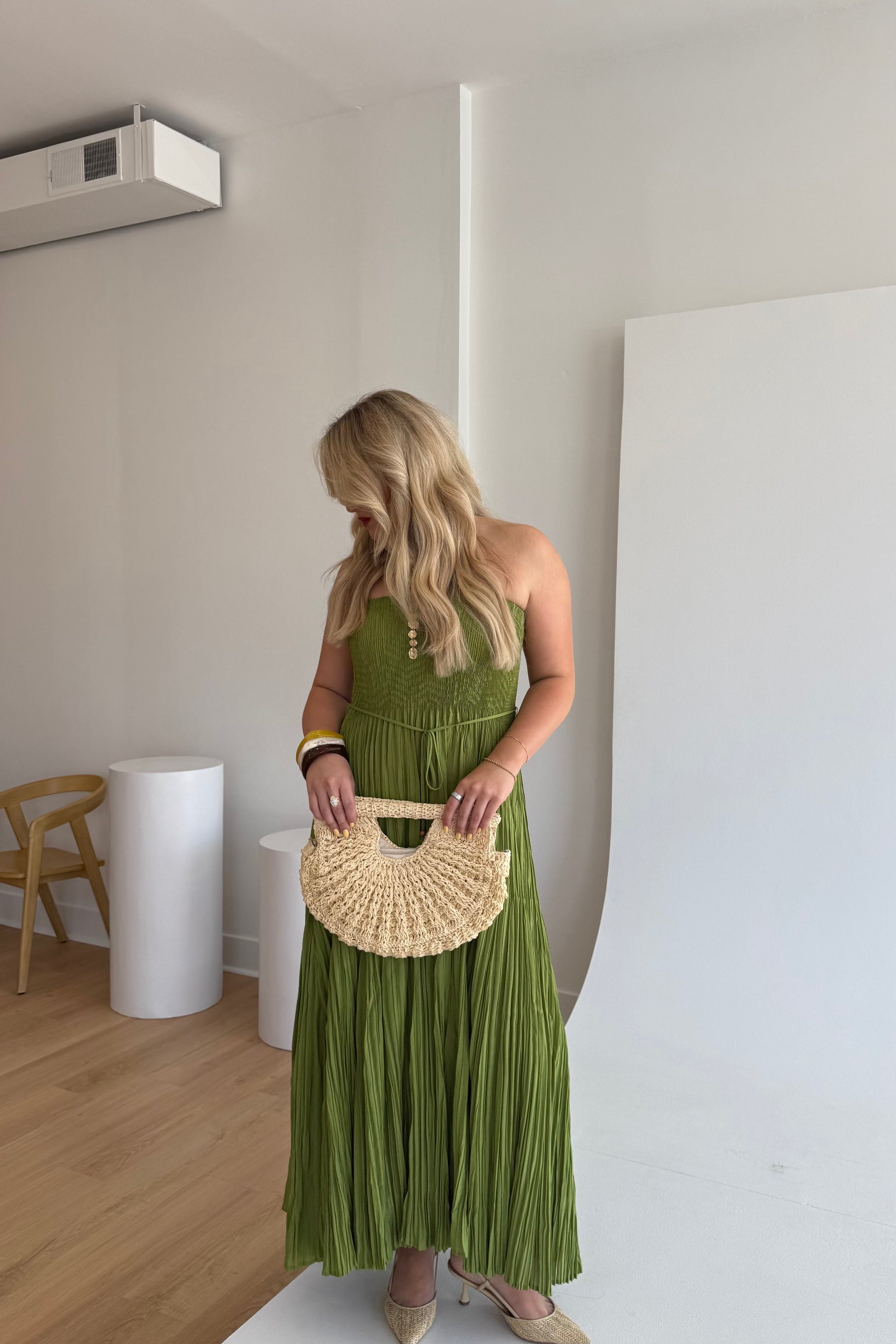 Woman in a green dress holding a woven handbag in an indoor setting.
