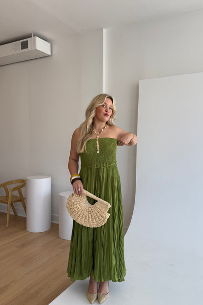 Woman in a green dress holding a woven handbag in an indoor setting.
