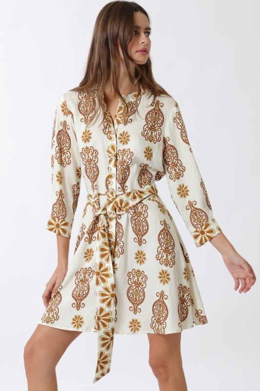 Woman wearing a cream-colored dress with brown floral patterns on a white background