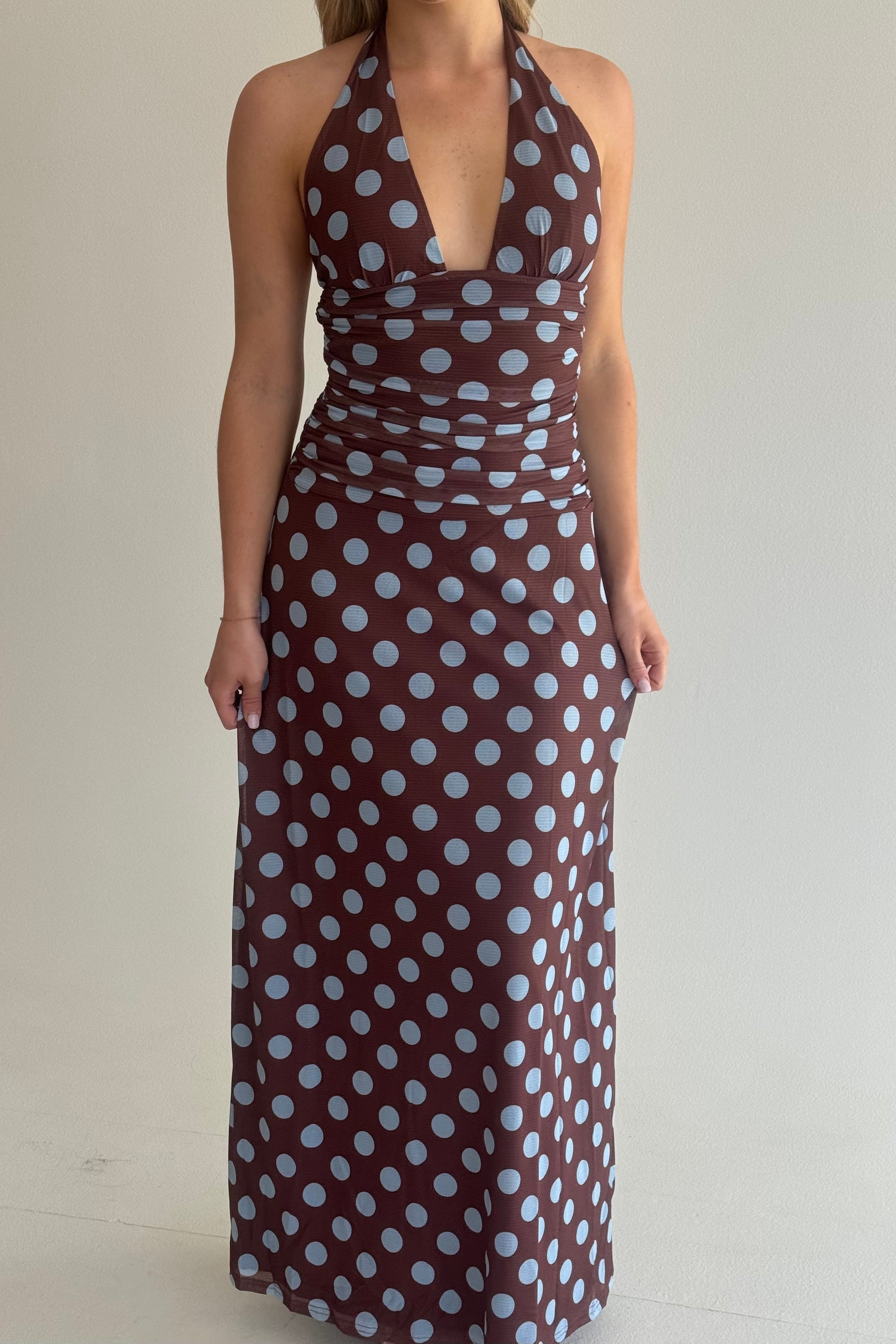 Woman wearing a brown dress with white polka dots against a plain background