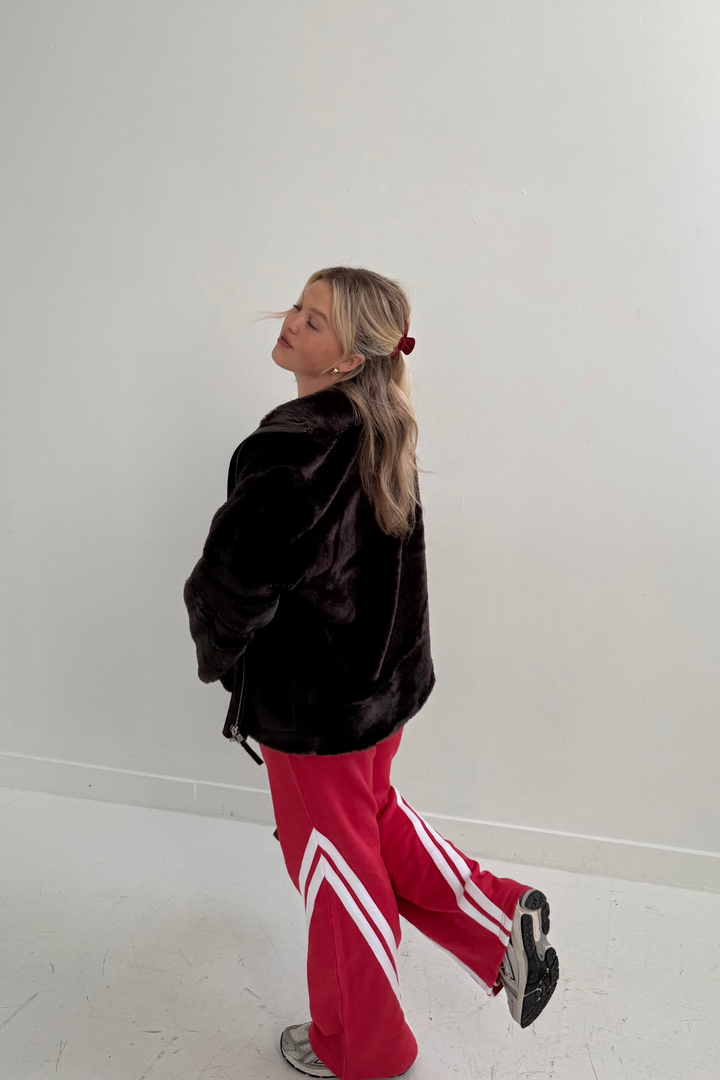 Model wearing a cozy black faux fur jacket with red track pants featuring white stripes.