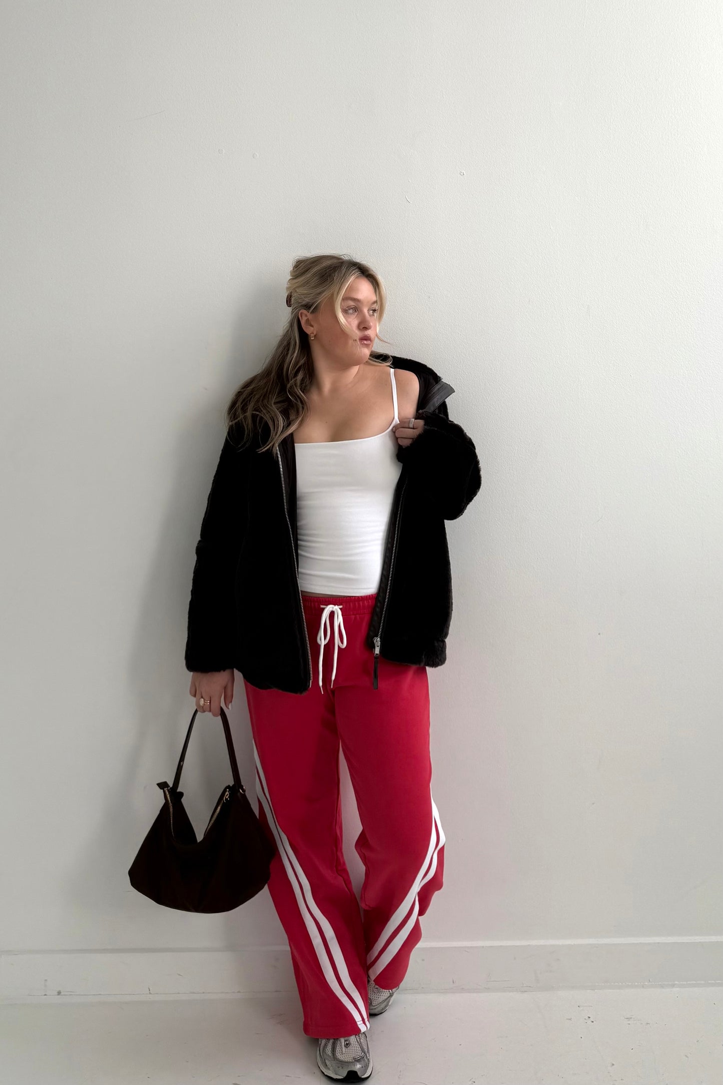 Model wearing a black fuzzy jacket, white tank top, and red sweatpants with white stripes.