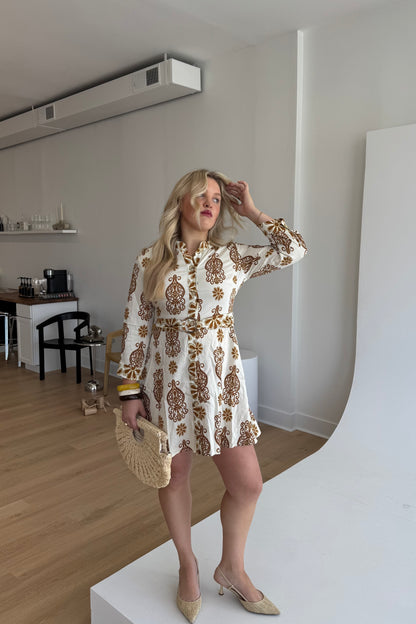 Woman in a patterned dress standing in a room with wooden flooring and white walls.