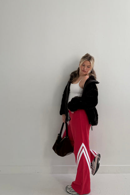 Casual women's outfit featuring black faux fur jacket, white tank top, and red track pants with white stripes.