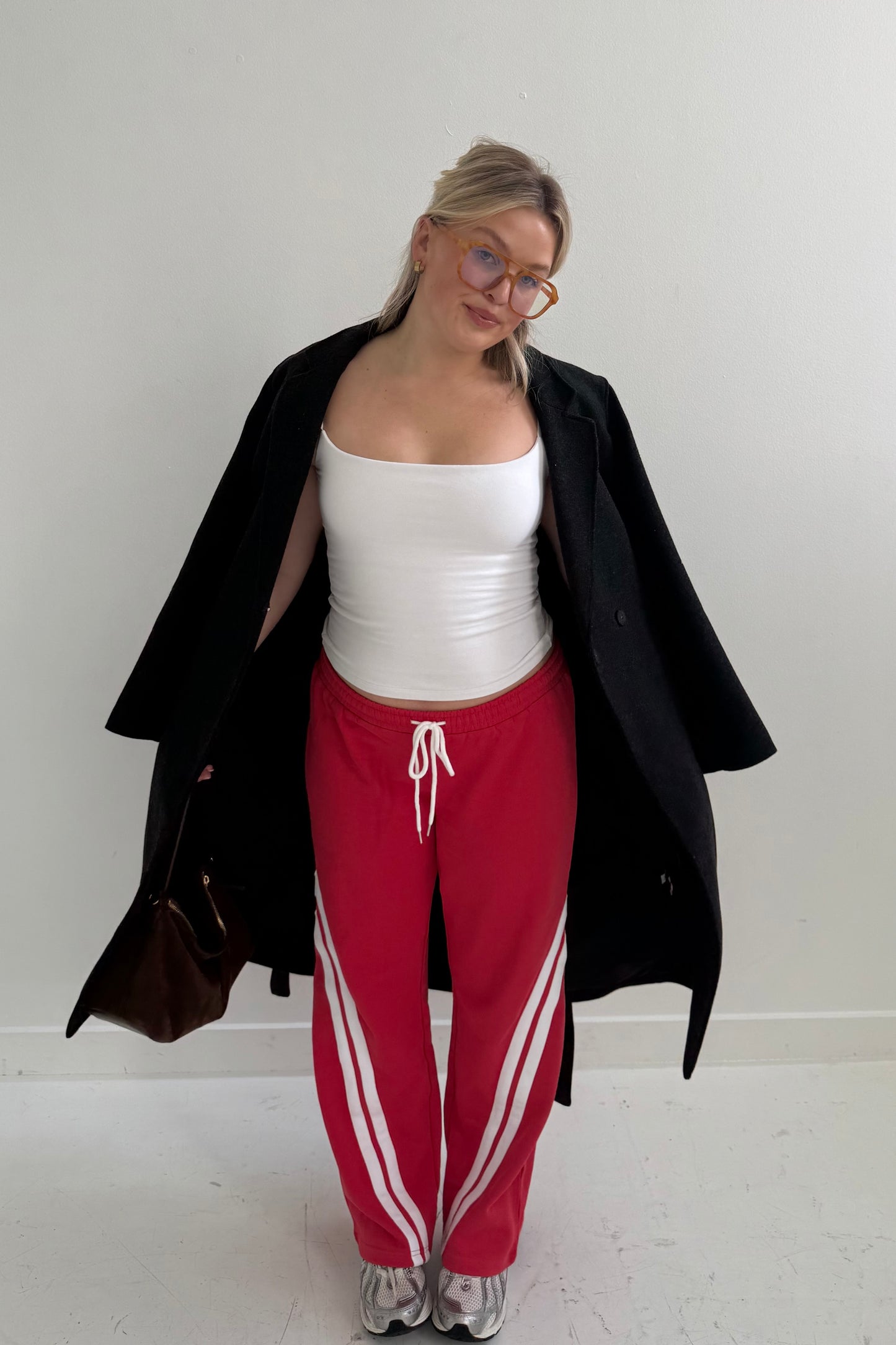 Casual outfit featuring a white tank top, red sweatpants with white stripes, and a black coat.