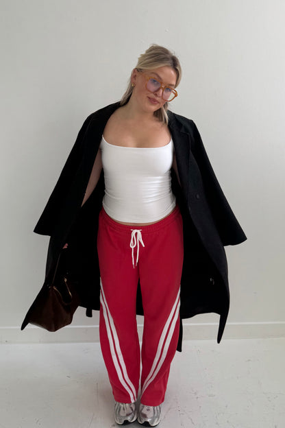 Casual outfit featuring a white tank top, red sweatpants with white stripes, and a black coat.