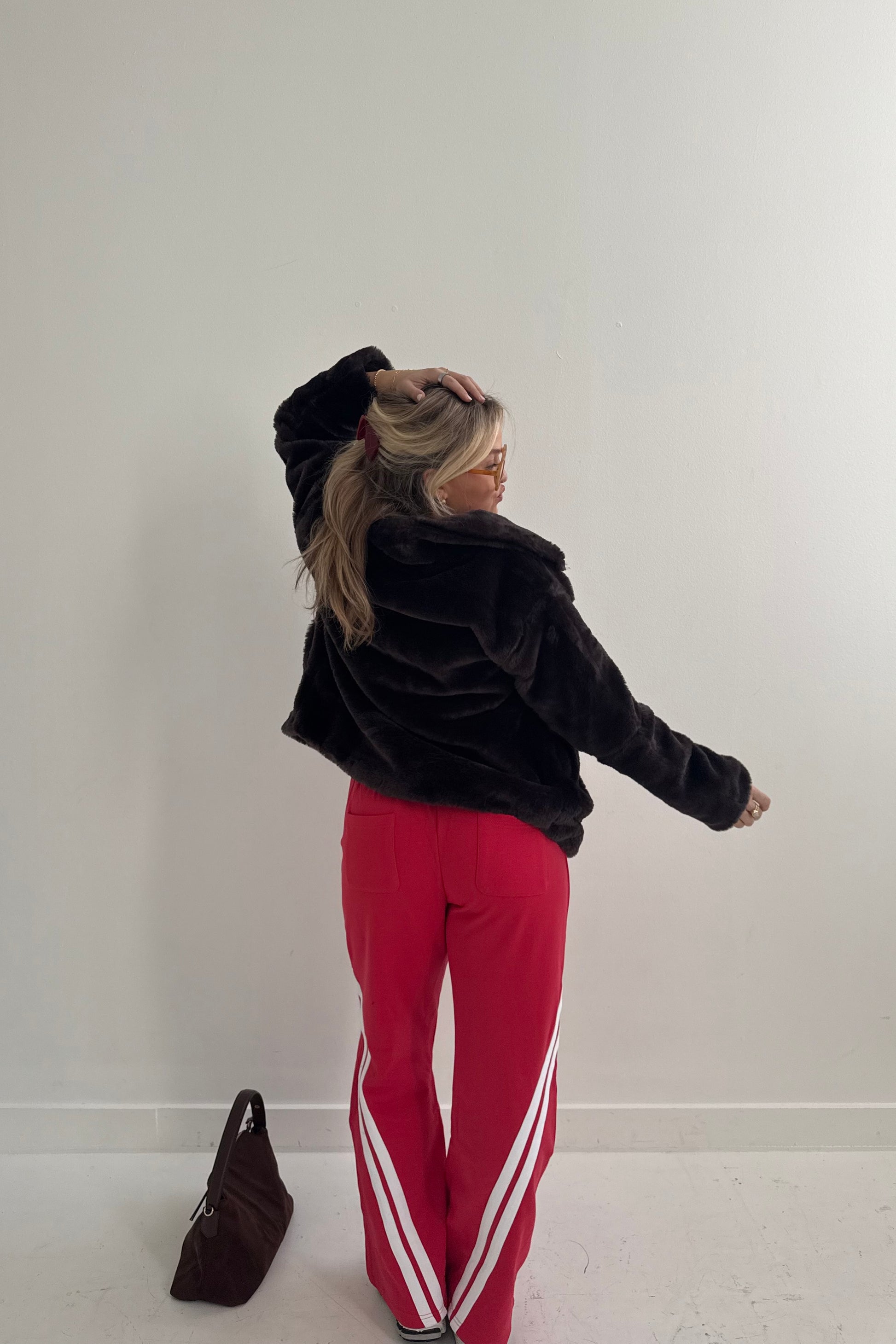 Woman wearing a brown faux fur jacket and red flared pants with white stripes, stylish casual outfit.