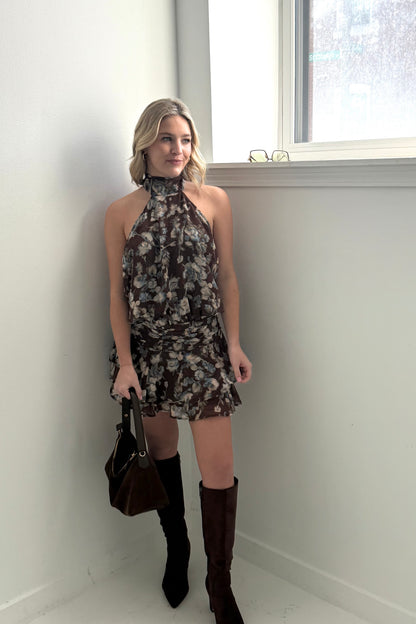 Floral halter neck dress in brown with ruffled skirt, paired with tall black boots and a handbag.