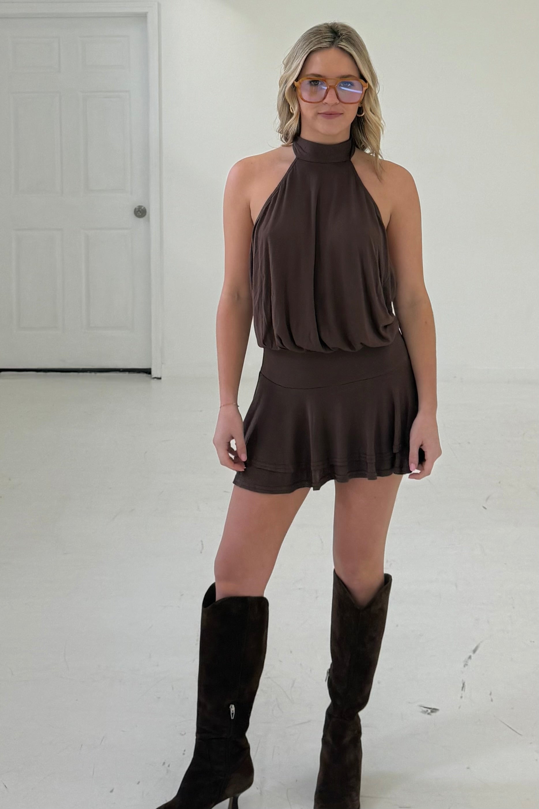 Brown halter neck mini dress in soft fabric, featuring a flared skirt and paired with knee-high boots.