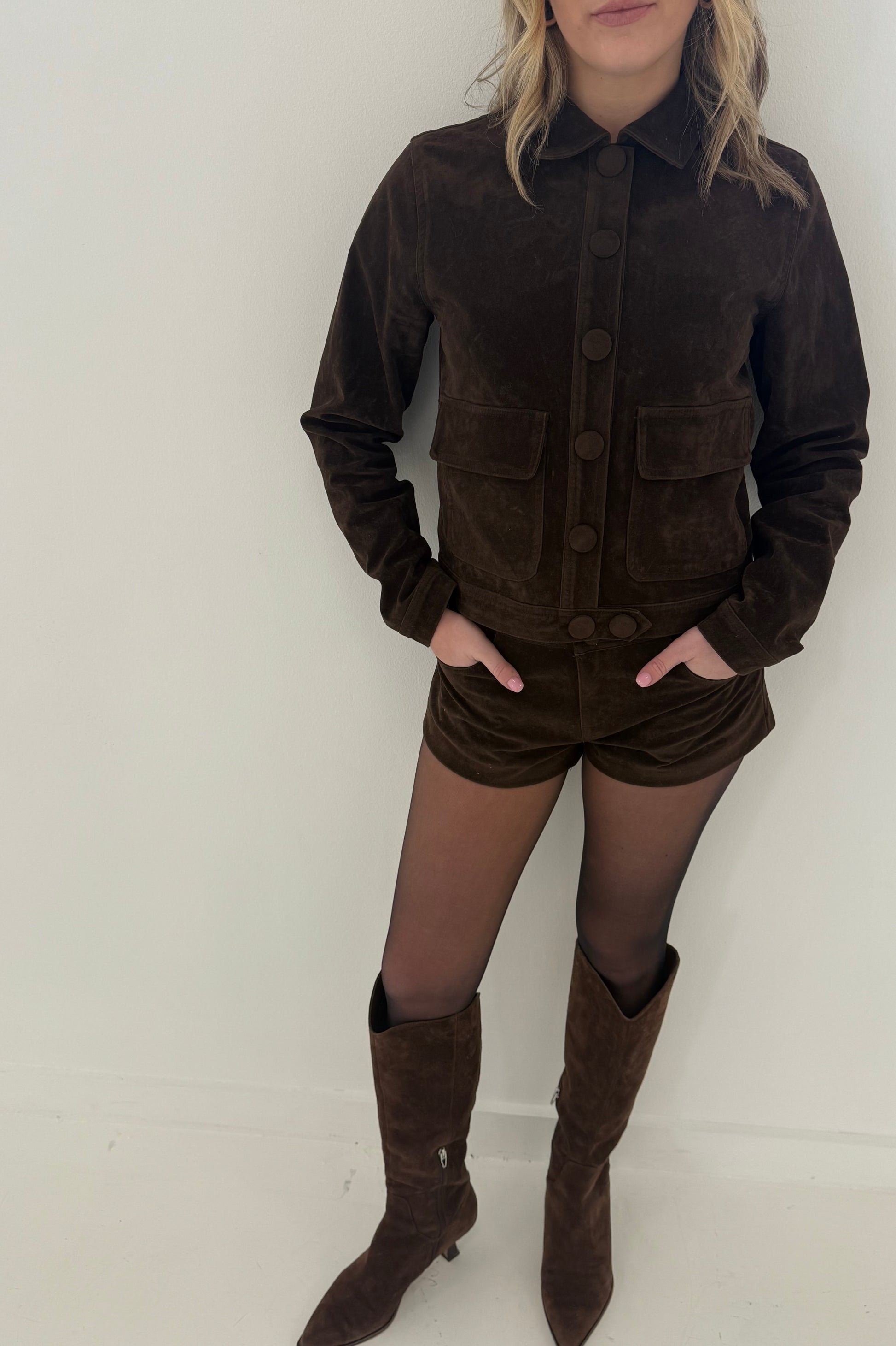Brown suede jacket with buttons and pockets, paired with matching shorts and knee-high boots.