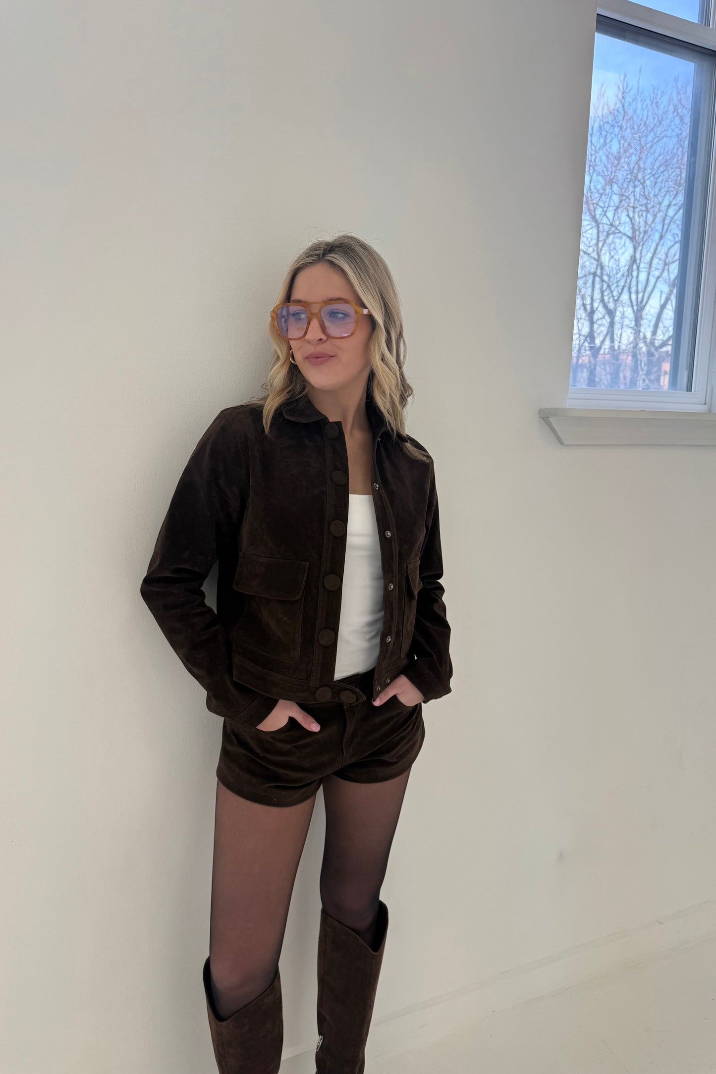 Brown suede cropped jacket with button closure, paired with matching shorts and knee-high boots.
