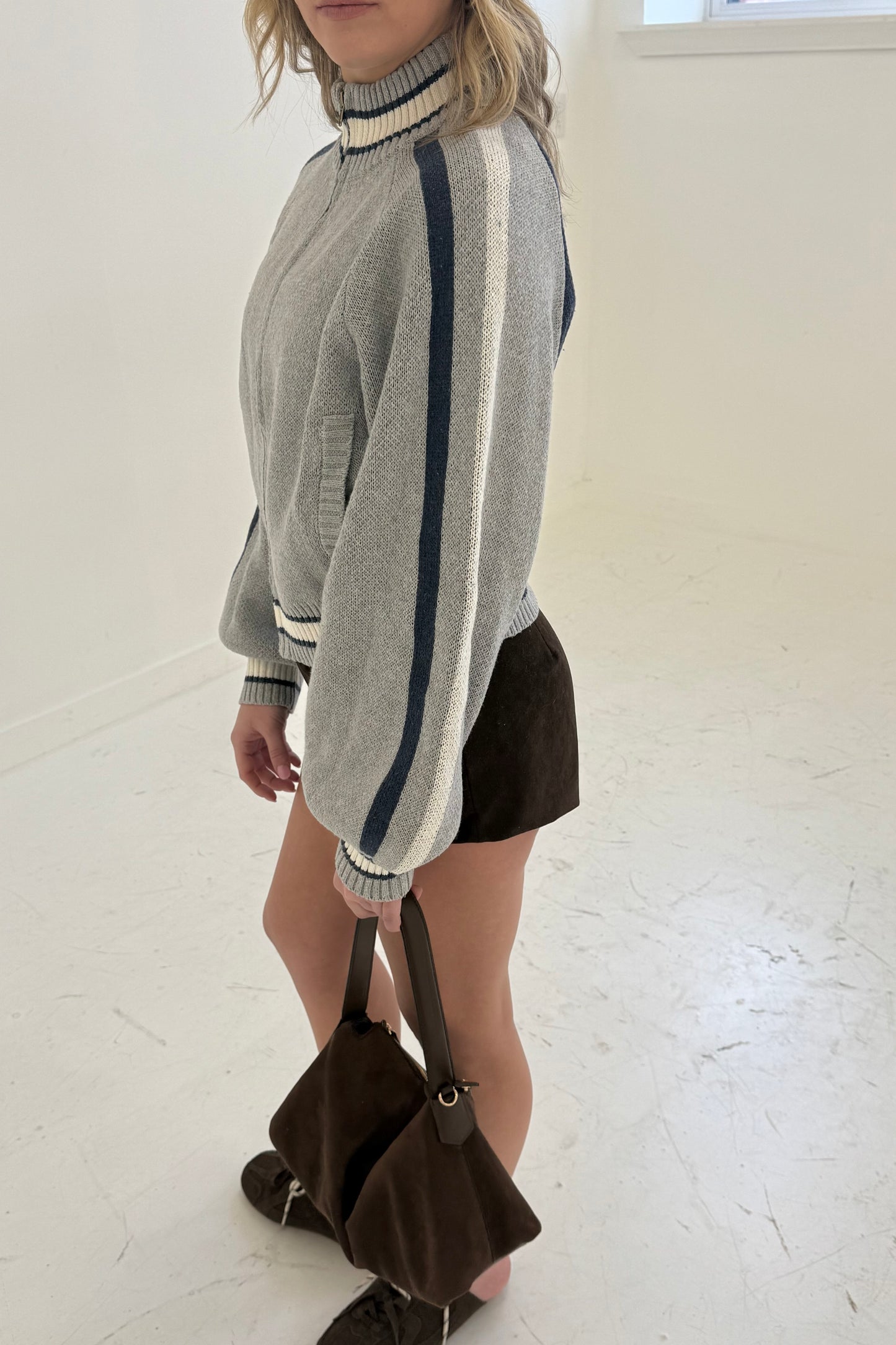 Gray zip-up sweater with navy and white stripes, paired with brown suede shorts and handbag.