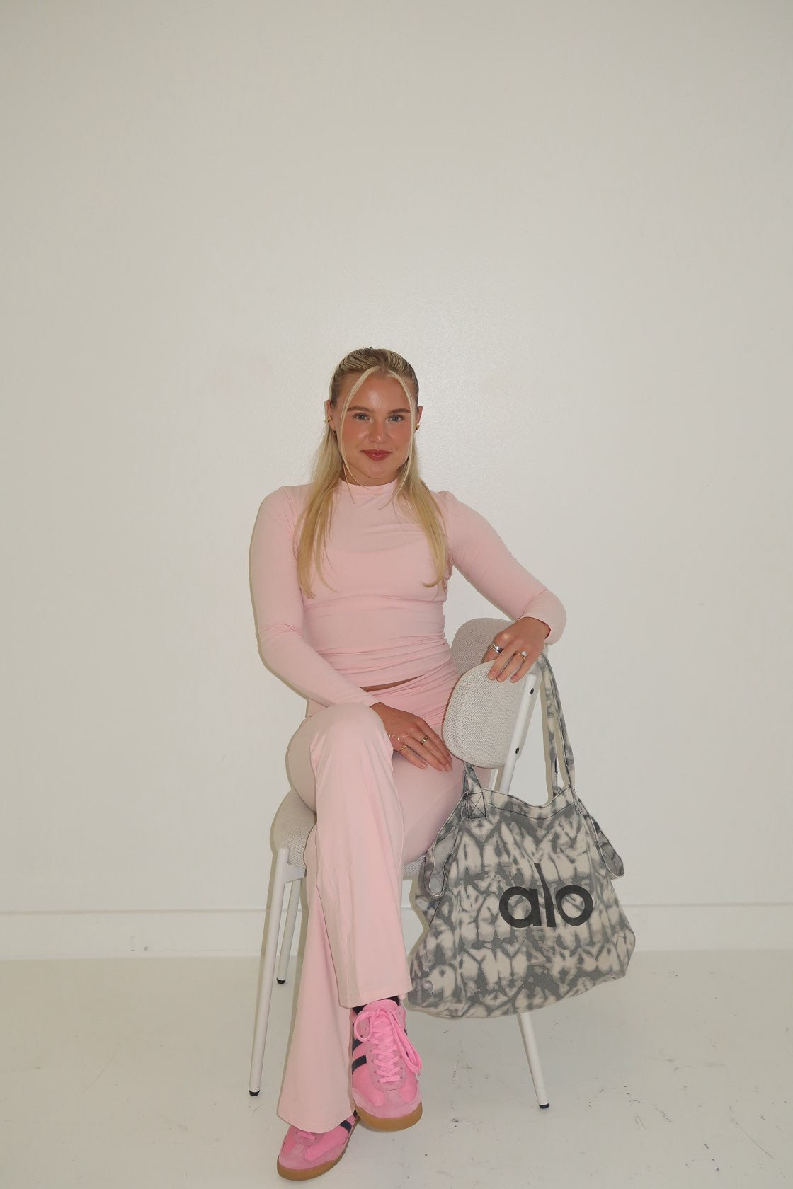 Person in pink outfit sitting on a chair with a patterned bag behind them.