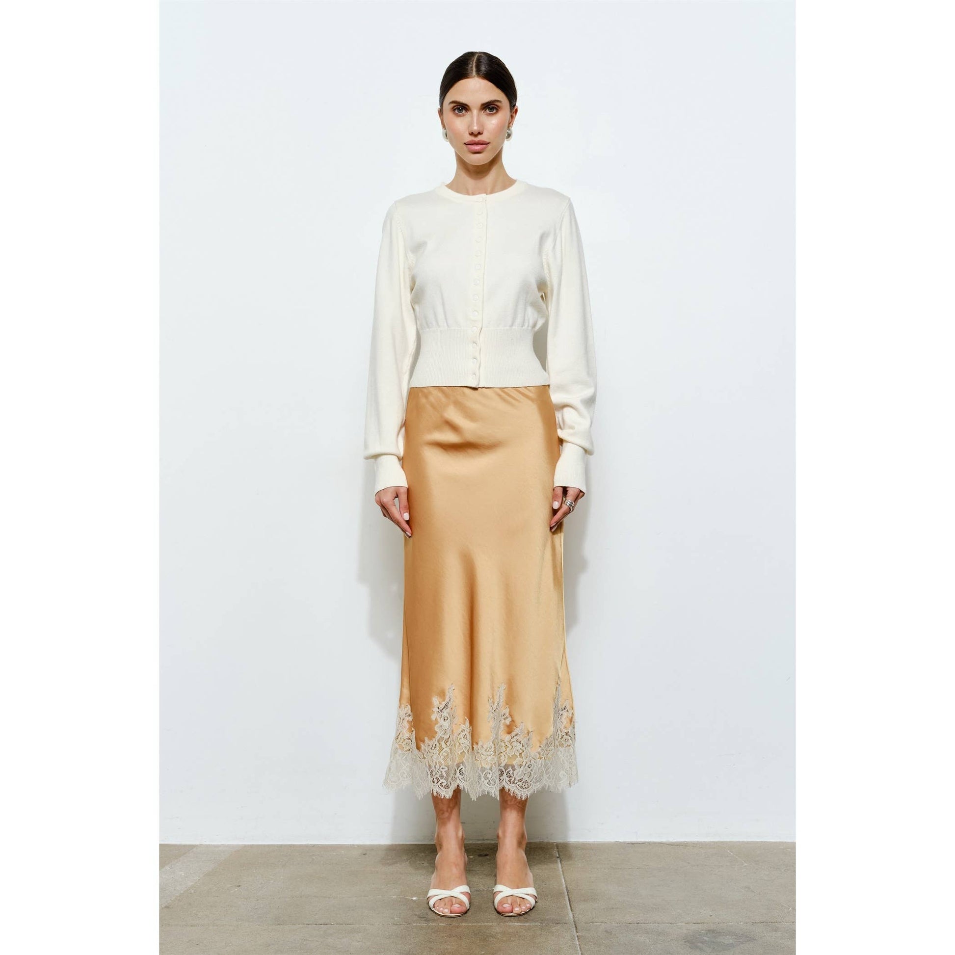 Elegant beige satin skirt with lace hem paired with a white cropped cardigan, perfect for chic occasions.