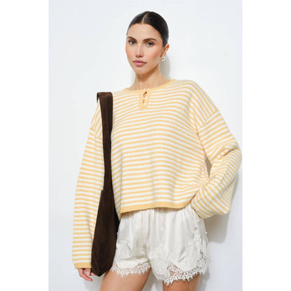 Woman wearing a yellow striped sweater and white shorts with a brown bag on a white background
